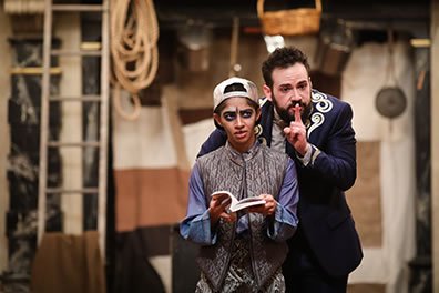 Production photo by Lindsey Walters, of the Ghost paging through a book and Leo leaning over his shoulder with a shushing finger to his mouth.